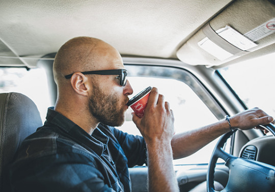 un homme en train de boire un café au volant de sa voiture