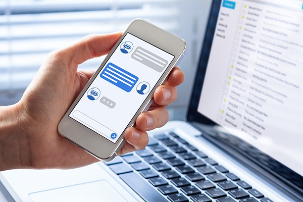 une main tenant un téléphone devant un pc protable