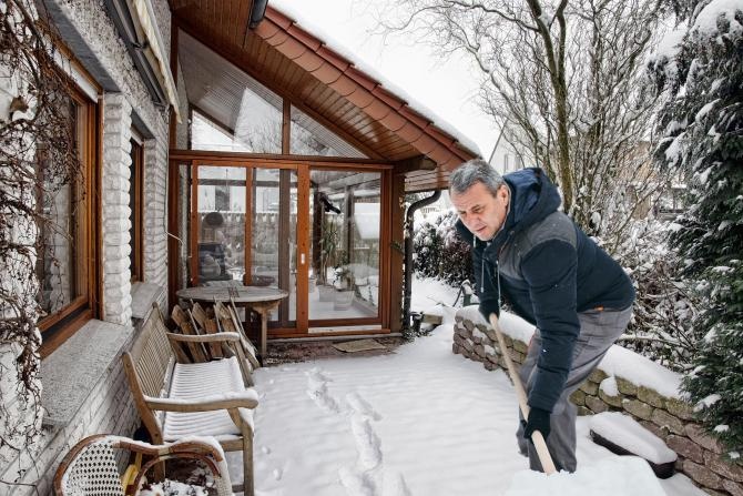 un homme en train de pousser la neigne de la terrasse d'une maison