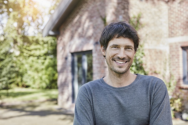 un homme souriant devant une maison