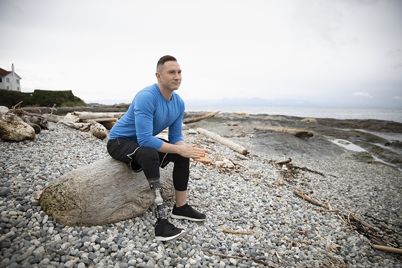 une homme avec une protèse à la jambe droite assis sur un rocher à la plage