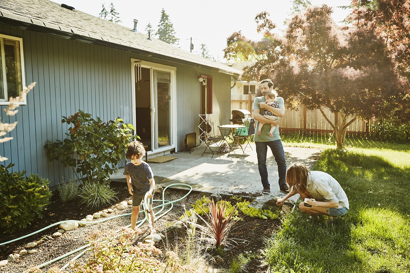un homme portant un enfant devant une maison et des enfants en train de jouer devant la maison
